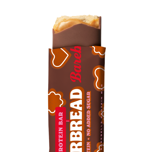 A Barebells Gingerbread soft protein bar partially unwrapped from a brown paper sleeve, showing a caramel-topped protein filling and the Barebreads branding on a white background.