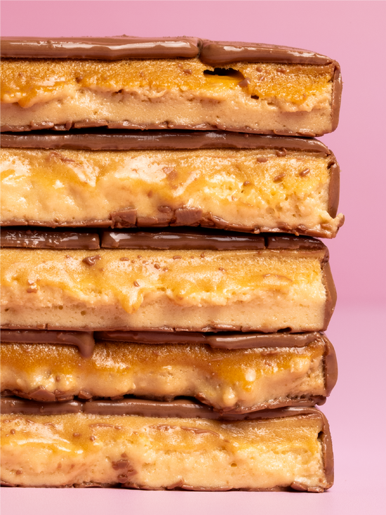 A close-up stack of five Barebells Gingerbread soft bars cut in half against a solid pink background.